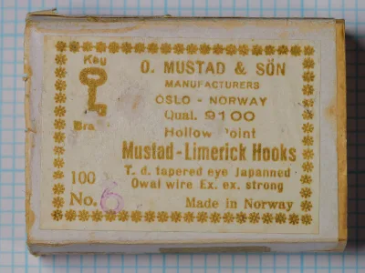 Mustad 9100 box label — O. Mustad & Son Oslo manufacturer packaging with gold letterpress text on cream cardstock, showing model, specifications, and 100-hook quantity marking