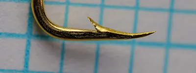 Mustad 92627 Flounder — hook specimen, upper angle view — gold-plated finish under raking light — shows wire forging texture and point taper