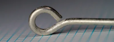 Mustad Gravitation size 15 — side view showing turned-up ball eye and bend profile — tinned finish on measurement grid