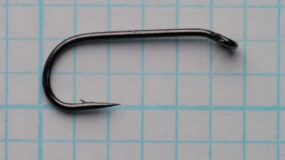 Side view of a dark single hook with a closed ring eye turned down, a round bend, a straight point and a small barb.