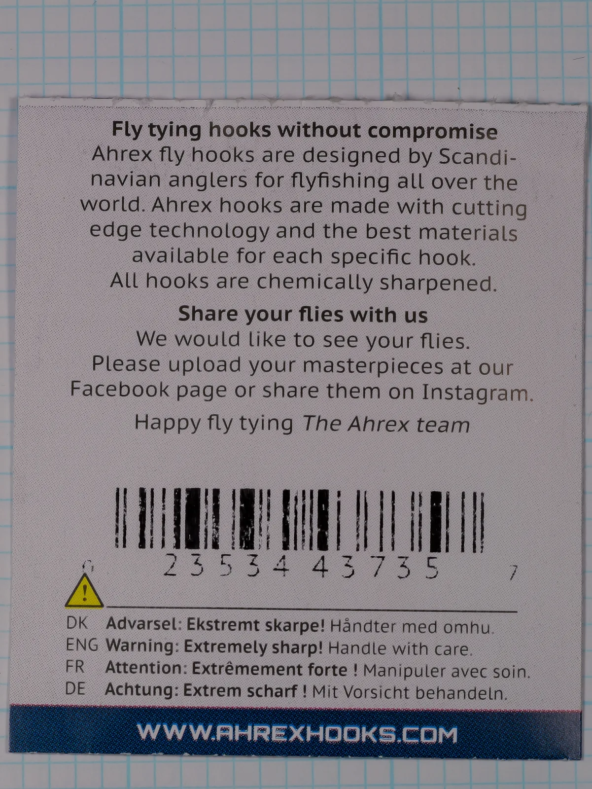 Back of a flat paper packet with two text blocks, a barcode, a yellow warning triangle and a dark blue band at the bottom.
