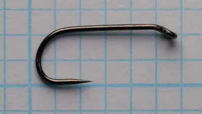 Side view of a black Ahrex FW501 size 12 hook lying flat on blue grid paper.