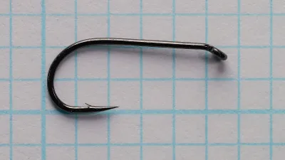 Side view of a black Ahrex FW502 size 12 dry fly hook on grid paper, with a straight shank, round bend, small barb and down-angled eye.
