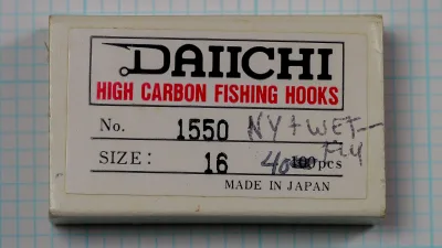 Cream cardboard box lid with a white label printed DAIICHI, HIGH CARBON FISHING HOOKS, No. 1550, SIZE: 16 and MADE IN JAPAN, with handwritten notes, on blue grid paper