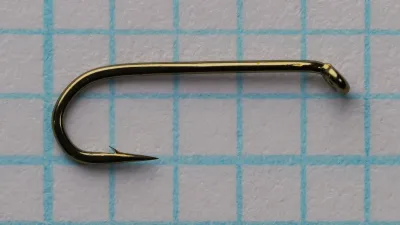 Side view of a size 16 hook on blue grid paper: straight plain shank, ring eye turned down, round bend, long point with a small barb, bronze-colored finish.