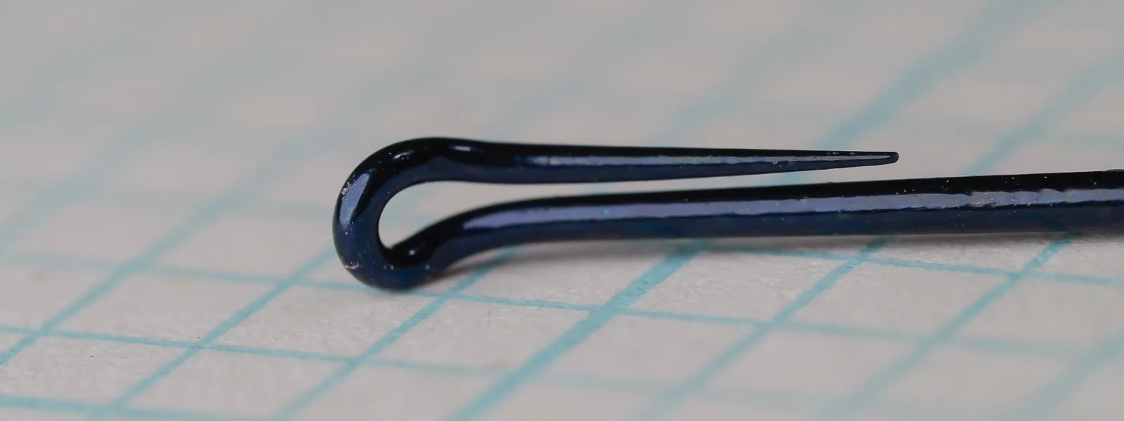 Close-up of the closed wire loop eye of a blue-black Daiichi 2139 size 6 hook on grid paper.