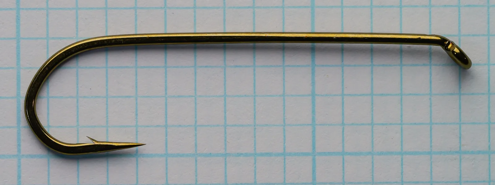 Side view of a bronze-colored size 4 streamer hook on graph paper, eye at right turned down, point at lower left.