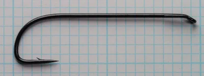 Black long-shank hook with a turned-down loop eye and barbed straight point, lying on blue grid paper.