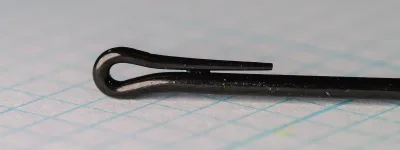 Close-up of a black hook eye: the wire end curls back into a teardrop loop, with a tapered tail lying along the shank.