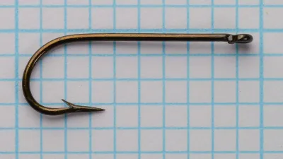 A whole hook lying flat on a grid, with a small ring eye, a straight shank, a round bend and a barbed tapering point.