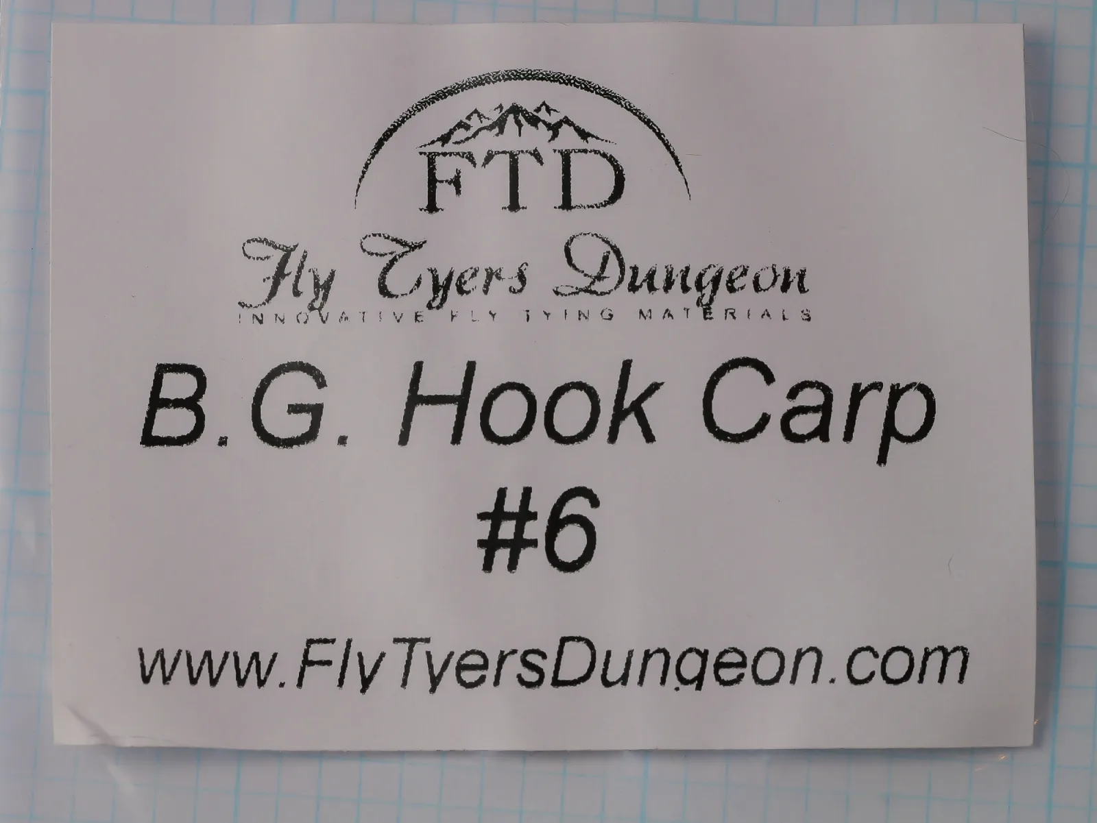 White paper label in a clear plastic packet, printed in black with the FTD logo, the Fly Tyers Dungeon wordmark, B.G. Hook Carp, #6 and the maker's web address.