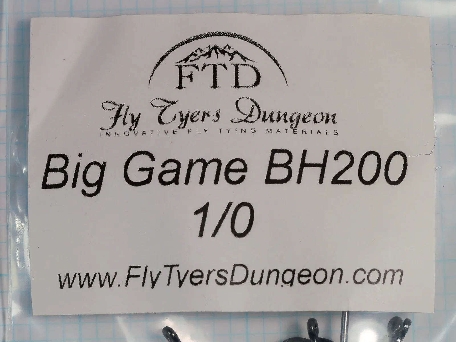 Paper label inside a clear plastic bag, printed with the FTD logo, Fly Tyers Dungeon, Big Game BH200, 1/0, and the web address, with hook eyes showing along the lower edge.