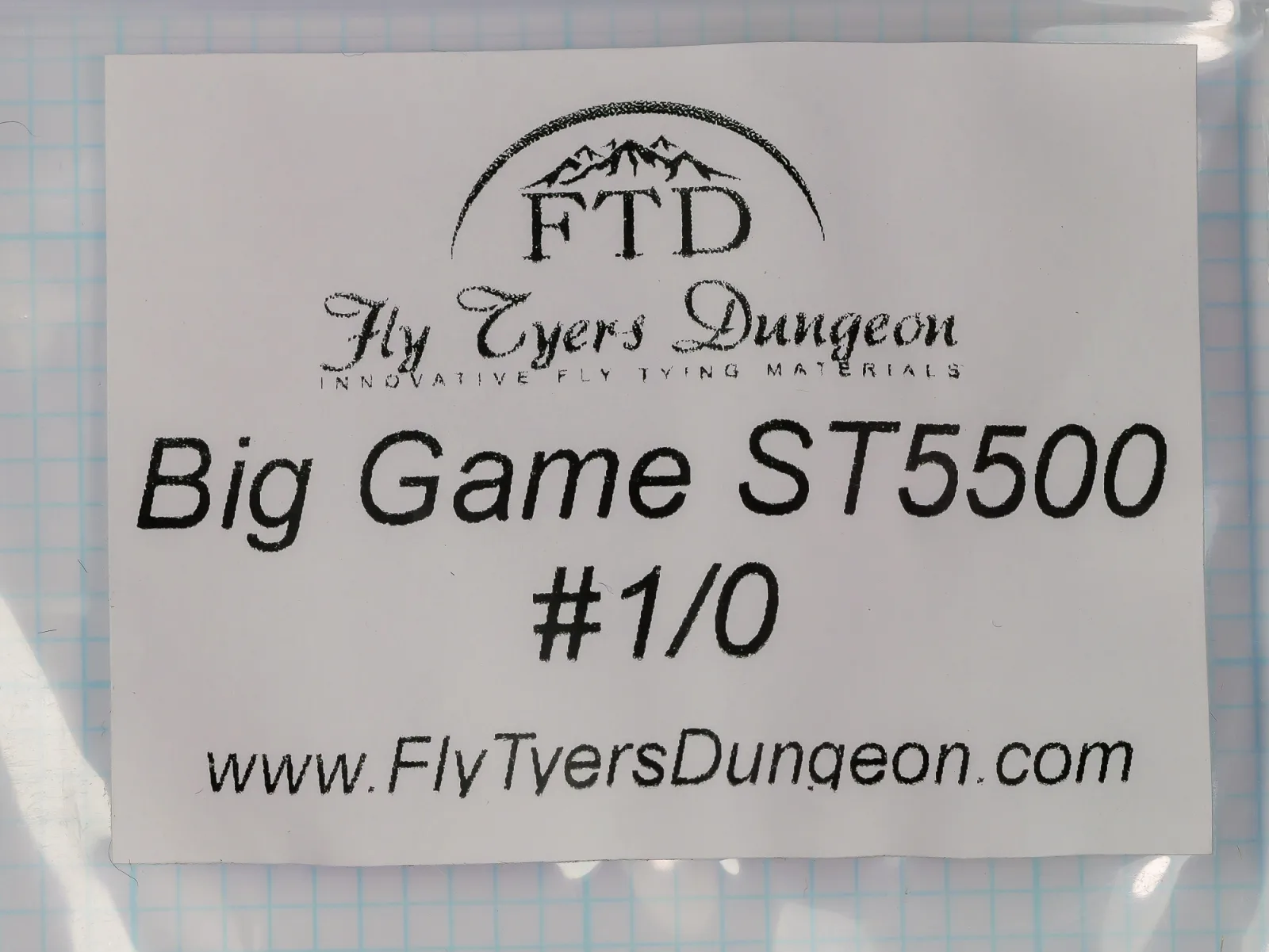 White paper label in a clear plastic bag, printed in black with the FTD logo, the script wordmark Fly Tyers Dungeon, and the lines Big Game ST5500 and #1/0.