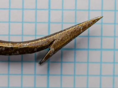 Close view of the hook point and barb on blue graph paper.
