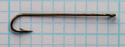 Side view of a dark brown-bronze hook on grid paper: straight shank, ring eye at right, deep round bend at left and a barbed point.