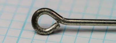 Close view of a ring eye on graph paper, the wire end bent back into a round loop with a hairline gap at the join.