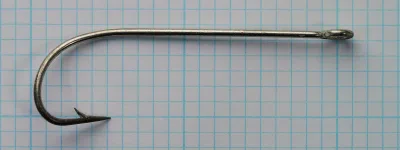 Side view of a single hook lying flat on graph paper: ring eye at the right, straight shank, wide rounded bend and a barbed point.