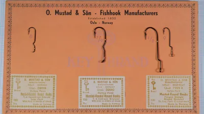 Orange Mustad Key Brand sales card with three gold-printed labels and four hooks tied on; the 7959 A label and two hooks stamped 1/0 and 9 are at the right.