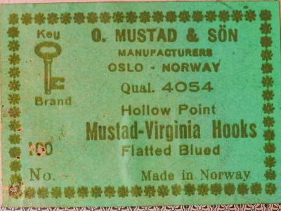 Green paper label printed O. Mustad & Sön, Qual. 4054, Hollow Point, Mustad-Virginia Hooks, Flatted Blued, Made in Norway, with a small key device at left.