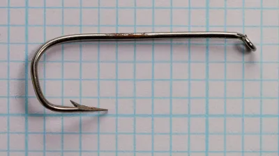 Mustad 9856 size 1 hook in side view on grid paper, with a rust-brown streak on the shank.