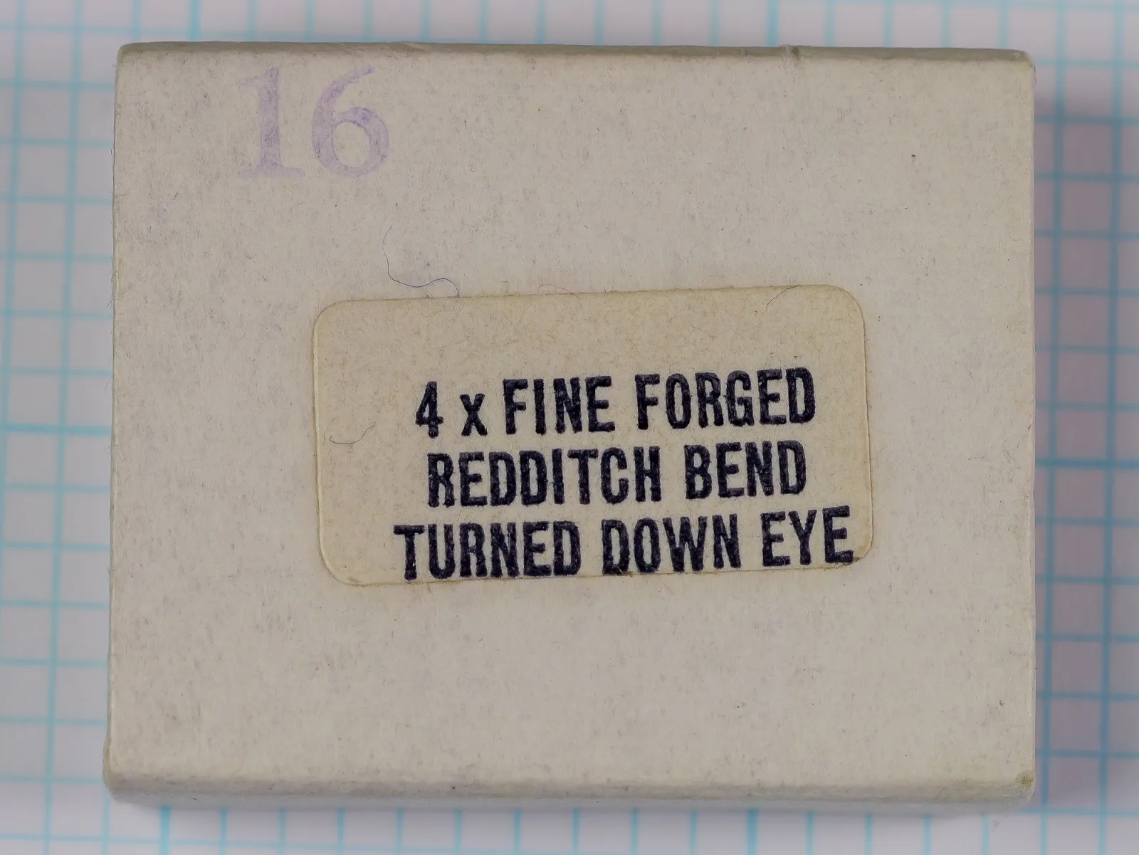 Gray-beige box lid with a pasted cream-white label reading 4 x FINE FORGED, REDDITCH BEND, TURNED DOWN EYE, and a violet 16 stamped at the upper left, on grid paper.