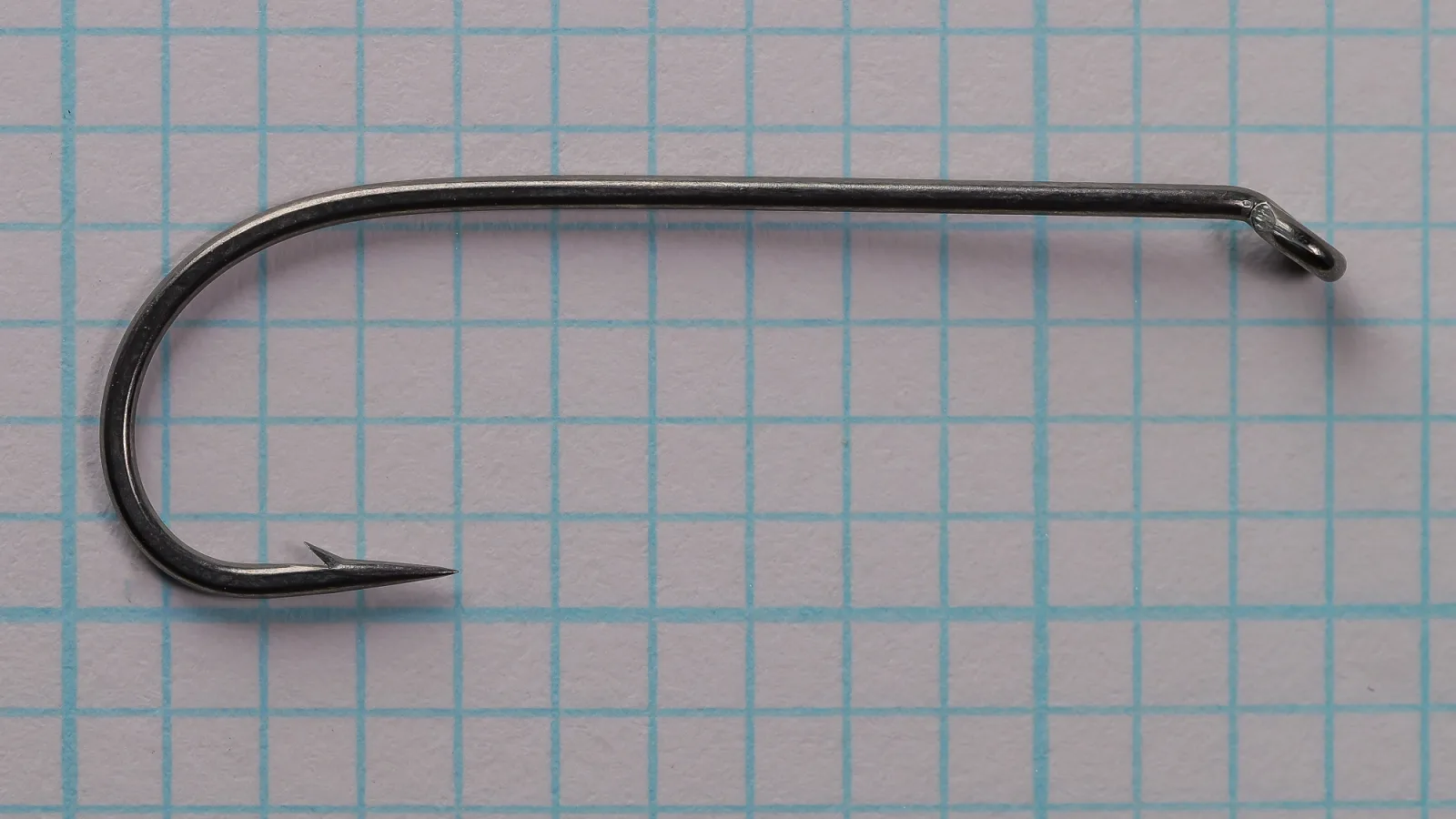 Side view of a size 4 Partridge CS11/1 hook on a grid: long straight shank, round bend, barbed point, turned-down ring eye, dark grey finish.