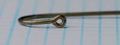 Low-angle close view of the loop at the point end of a size 10 Tag hook, with a small nub on its underside, on grid paper.