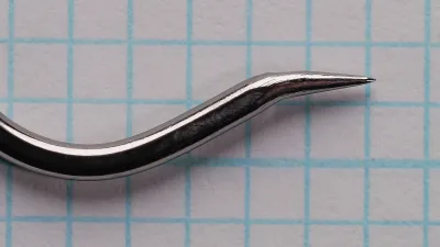 Close view of a tapered hook point with a fine tip and no barb, following an S-shaped curve from the bend, on blue grid paper.