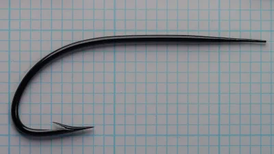 Glossy black blind eye salmon hook with a long, gently arched shank and broad sweeping bend, on blue grid paper.